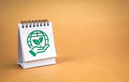 Earth day, world care and green environmental sustainability concepts. Earth care symbol, hand holding global, on white desk calendar standing isolated on recycle paper background with copy space.の写真素材
