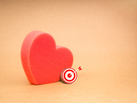Love match, couple finding mission, matching partners online concept. Small red 3d target icon ig red bold sponge heart shaped, isolated on recycle kraft paper background with copy space.の写真素材