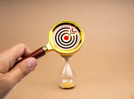 Short-term business goals encompass work that helps an organization reach its mid-term goals concept. Target icon in gold magnifying glass lens in hand while zoom in at hourglass on brown background.の写真素材