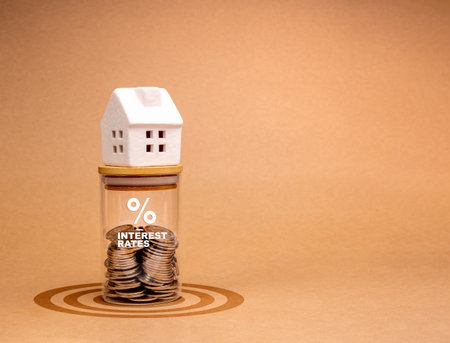 Mortgage interest rates, home Tax, property financial concepts. Miniature white house on glass bottle with percentage icon and text "INTEREST RATES", coins inside, on target symbol, brown background.の写真素材