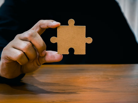 A jigsaw puzzle in businessman hand. Man in black shirt showing empty piece of important jigsaw puzzle on wood desk. Business solution and idea, partnership, elements of career success part concept.の写真素材