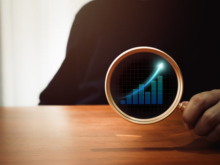 Business analytic chart, digital growth graph icon in round lens of gold magnifying glass in businessman's hand on dark background. Trends searching, money stock trading analysis, investment concepts.の写真素材