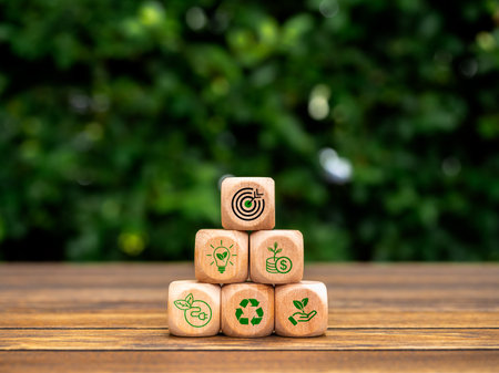 Green business management process and environment conservation concept. Target icon and saving energy strategy symbol on wooden cube blocks pyramid stack on wood table on blur green leaves background.の写真素材