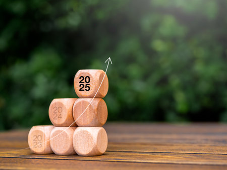 Rise up arrow on wooden cube blocks stack, business growth graph steps with 2025 year number on wood table on green leaves background with copy space. Green business growing and environment concept.の写真素材