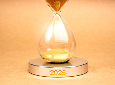 Coming soon to new year 2025, business and technology concept. Close-up hourglass with gold sand inside, on round silver chrome podium with 2025 year calendar number on brown background, minimalist.の写真素材