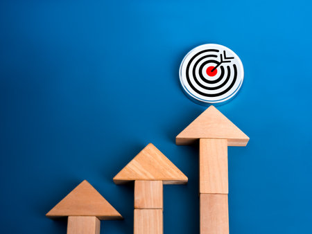 Business trends and growth success target goal concept. Big target icon, o round chrome badge hit by arrows, arrange by wooden blocks as growth graph diagram on blue background, minimal and eco style.の写真素材