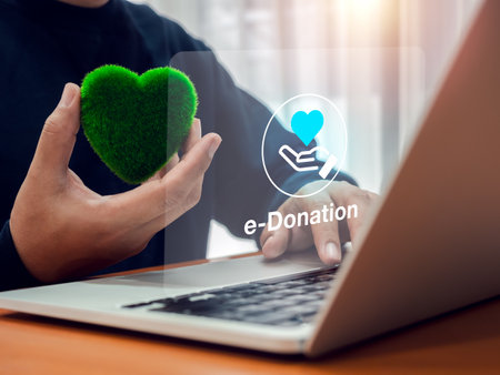 Donation online concept. e-Donation website screen with hand hold heart icon, charity and fundraising, appear on virtual screen on laptop while person hands holding green grass heart shape ball.の写真素材