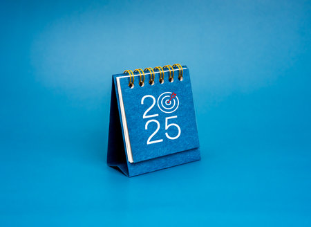 Happy new year 2025 background. 2025 year numbers with target icon on blue small desk calendar cover standing isolated on blue background, minimal style. Business trend, goals and success concept.の写真素材