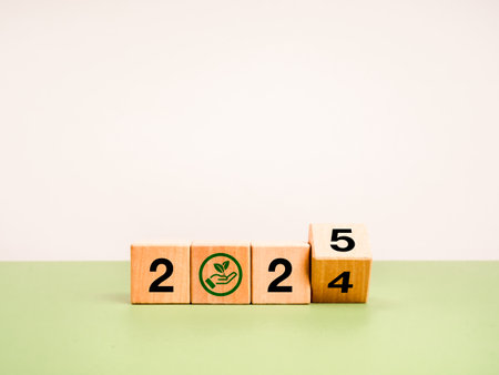 Happy new year 2025 with earth and environment care concept. Flipping wood cube block with 2024 change to 2025 calendar numbers with hand hold leaf icon on green table and white background, minimal.の写真素材