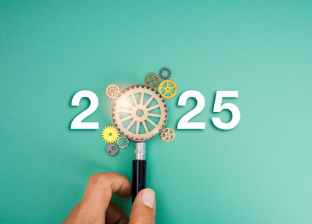 Happy 2025 new year with business goals plan and management concept. 2025 calendar numbers decoration with target icon in magnifying glass lens in hand with many gears, cog wheels, green background.の写真素材