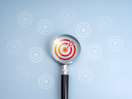Business trends and goals, right target searching, looking for the real goal concepts. Red bullseye icon focus by magnifying glass lens surrounding white dart boards on light blue background.の写真素材