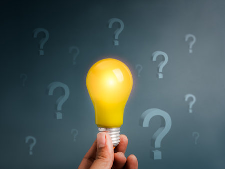 Innovative technology and idea management, solution, creative thinking, inspiration, and problem solving concept. Glowing yellow light bulb holding by person, surrounded with question mark symbols.の写真素材