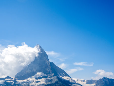 Background of blue sky with the great Matterhorn in the Swiss Alps. Amazing view of pyramidal peak of Matterhorn with white puffy cloud, tourist destination with summer mountains in Switzerland.の写真素材
