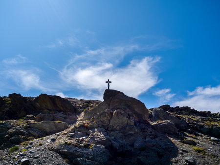Black cross standing on top of cliff rock formation on blue sky background. Silhouettes of cross standing on the otp of the cliff, at tourist trail view with mountains in Zermatt, Switzerland.の写真素材