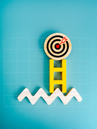3d Target icon on round wood badge on top of yellow ladder on zigzag line, on graph grid, blue background, vertical style. Business market growth, goal and success, investment planning concept.の写真素材