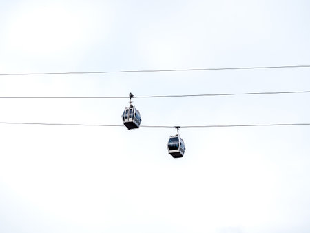Two modern metallic cable cars cabins cross each other on the wires, cableway blue sky background...