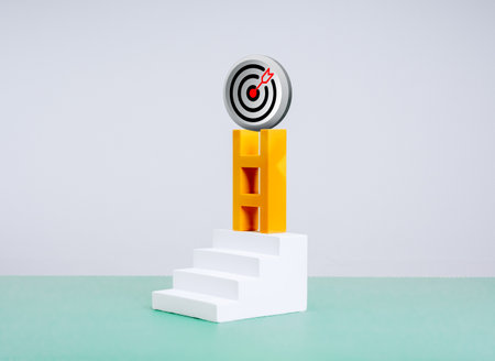 3d modern target dartboard bullseye icon on top of yellow ladder, on stair steps on green table, white background. Business market growth, marketing goal, efforts towards goals, leader vision concept.の写真素材