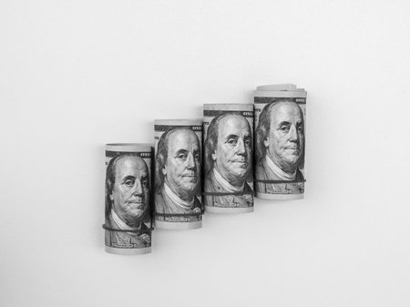 Four rolled of one hundred dollars bill banknote, with rubber band, arranged as a graph step, isolated on white background. Money cash, business financial and foreign currency investment concept.の写真素材