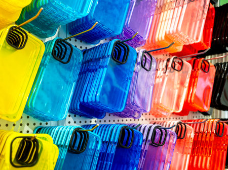 Transparent multicolor of back covers for smartphone. Colorful fluorescent mobile phone case with empty space for camera lens, hanging on hooks on shelf, white wall in the mobile accessories shop.の写真素材