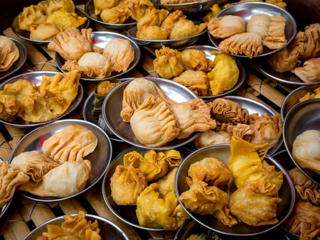 Many oriental crispy deep fried wontons in small stainless steel mini bowl preparing in local restaurant, Chinese dim sum takeaway finger food. Fried halal chicken wontons, tasty breakfast background.の写真素材