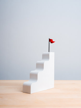 Red win flag on top of white staircase as bar graph chart steps on wood table, white vertical background. Business growth process, profit and investment, mission and success, leadership plan concepts.の写真素材