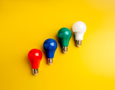 Creative idea, innovation technology, power and energy concept. Red, blue, green and white colors of glowing light bulbs arrange as growth graph steps, isolated on yellow background, minimalist.の写真素材