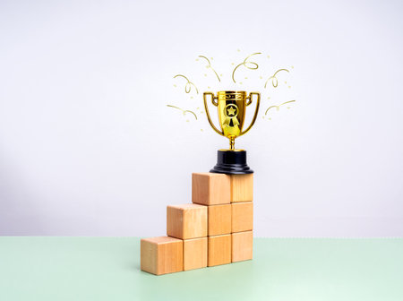 Gold star award trophy on top of wood cubes as bar graph chart steps on green table and white...