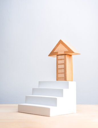 Wood block arranged as arrow on top of white geometric stair on wood table and vertical grey background. Business market growth, mission, goal and success process and economic improvement concepts.の写真素材