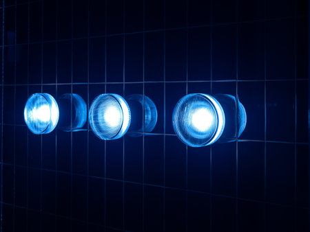 Three modern round blue light lamps, circle shape mounted on striped grid pattern dark black net grid line pattern wall background in the bathroom. Abstract cool lighting design, retro style concept.の写真素材