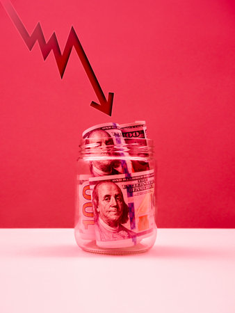 Fluctuating arrow shoots fall down at US dollars bill banknotes money cash inside glass jar on...