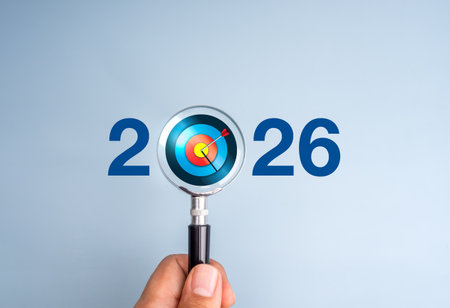 Happy new year 2026 banner, business goal and success, resolutions, success planning focus concept. Target icon inside magnifying glass lens in hand with 2026 calendar year numbers on blue background.の写真素材