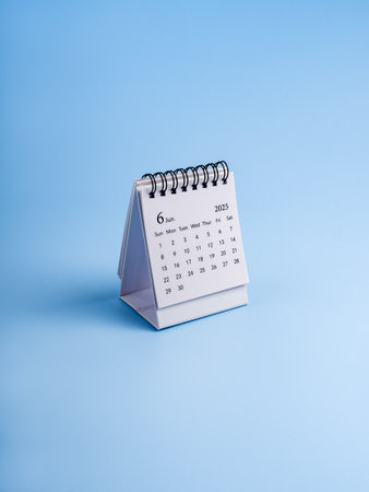 June, 2025 year page of desk calendar, organizer to plan and reminder standing isolated on blue vertical background, minimal style. White small table calendar with days, weeks and month numbers.の写真素材