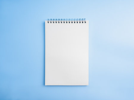 Blank vertical notepad isolated on horizontal blue background. Empty white paper, spiral notebook page template, mockup space for write, draw, short note, memo, creative ideas, inspirations.の写真素材