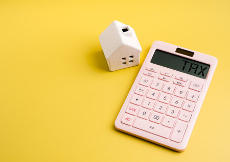 Property tax, real estate interest rates, home financial planning concept. âTAXâ on display of pink calculator and miniature white house model on yellow background with copy space, minimalist.の写真素材