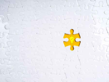 Missing puzzle piece with glowing light bulb icon on yellow background symbolizes finding the right idea, creative solution, problem solving, innovation, or strategic thinking for business success.の写真素材