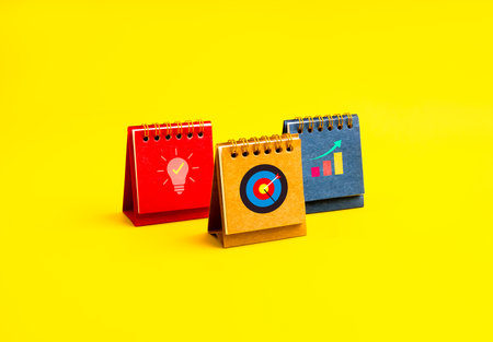 Business growth, strategic planning, goal setting, creative ideas, startup concept. Colorful desk calendars with icons, idea light bulb, target dart, and growth chart, isolated on yellow background.の写真素材