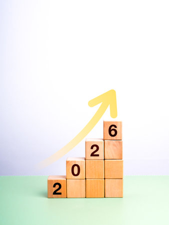 2026 new year business growth, future success, and strategic planning concept. Upward arrow on wooden cube blocks arranged as stairs steps with 2026 calendar numbers on green table, white background.の写真素材