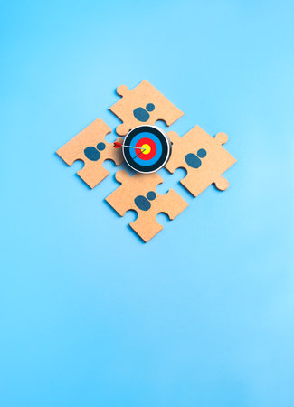 Teamwork concept with jigsaw puzzle pieces with human icons and target symbol on blue background, representing stakeholder alignment, cooperation, business goal, synergy, collaboration, team building.の写真素材