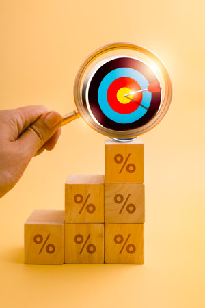 Hand holding magnifying glass focusing on 3d target icon above wooden percentage cube blocks as growth graph, symbolizing business growth analysis, marketing strategy, and goal achievement concepts.の写真素材