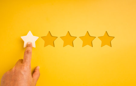 Hand pressing one star out of five on yellow background. Concept of ratings, customer review,...