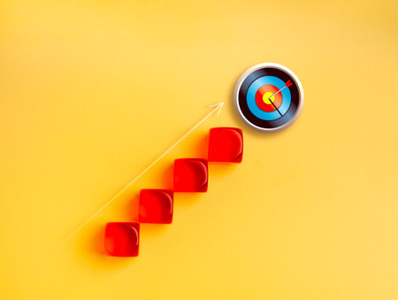Red blocks forming upward stairs leading to 3d target with arrow hit bullseye on yellow background. Concept of business growth, goal achievement, career success and strategic milestones planning.の写真素材