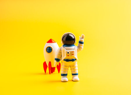 Toy astronaut with rocket on yellow background, symbolizing space exploration, startup innovation, future technology, childhood dreams, imagination, leadership, and creative business growth concept.の写真素材