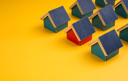 Stand out from the crowd concept with one red wooden house among many blue homes on yellow background. Home selection, real estate value, uniqueness, housing market, and property investment decisions.の写真素材