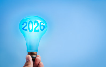 Hand holding glowing blue light bulb with 2026 number inside, representing new year technology...