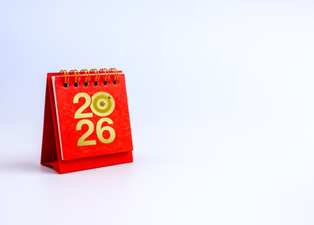 Red desk calendar with golden 2026 numbers and target icon with copy space symbolizing new year goal...