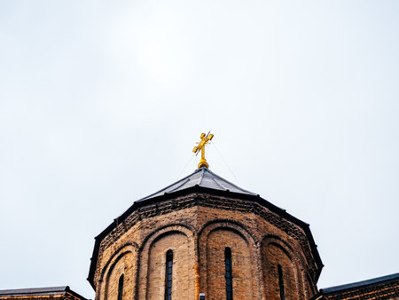Golden cross atop a traditional brick church dome in Tbilisi, Georgia, representing Orthodox faith,...