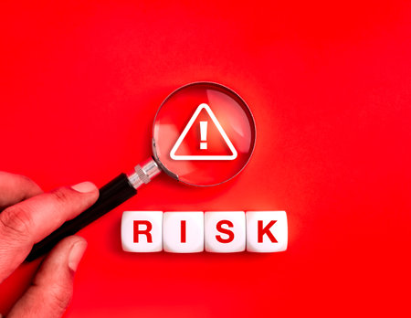 Magnifying glass focusing on warning sign and word RISK on red background. Concept for cybersecurity, data protection, online scam alert, fraud detection, financial risk, and safety awareness.の写真素材
