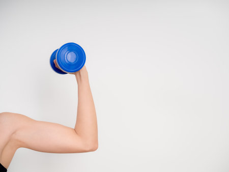 Strong female arm lifting blue dumbbell in isolated white background, symbolizing fitness, strength training, healthy lifestyle, and women empowerment through workout and gym exercise concepts.の写真素材