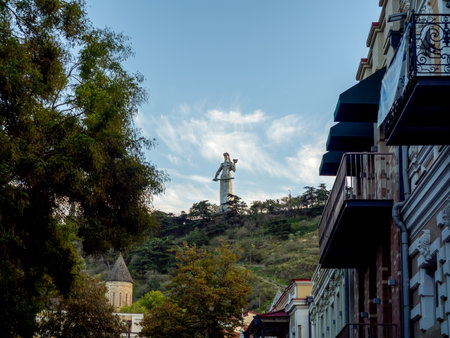 Distant view of the Mother of Georgia statue from city streets of Tbilisi, Georgia, with residential buildings, greenery, and soft evening light blending culture and urban scenery beautiful.の写真素材