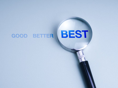Magnifying glass highlighting the word "BEST" from a sequence "GOOD, BETTER, BEST" on blue background, symbolizing excellence, improvement, strategic planning, work development, and decision making.の写真素材